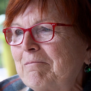 Maria aus Tübingen-Kilchberg überlebt einen Herzinfarkt dank Nachbarn. Sie trägt eine rote Brille und schaut gerührt.