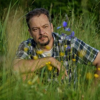 Naturfilmer und -schützer Jan Haft sitzt in der Hocke in einer blühenden Wiese.