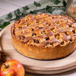 Rezept für Apfelkuchen mit Gitter: Goldbraun gebacken und sehr fein angerichtet steht der saftige Kuche auf einem Tablett. Äpfel liegen daneben.
