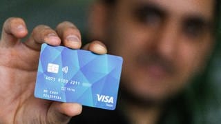 Baden-Württemberg, Offenburg: Ein Geflüchteter hält eine Debitcard in der Hand. 