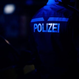 Ein Polizist vor einem Polizeiauto bei Nach (Symbolbild). Der Helm-Räuber überfällt zum zweiten Mal Tankstelle - zuerst Neckarsulm, jtzt Untergruppenbach.