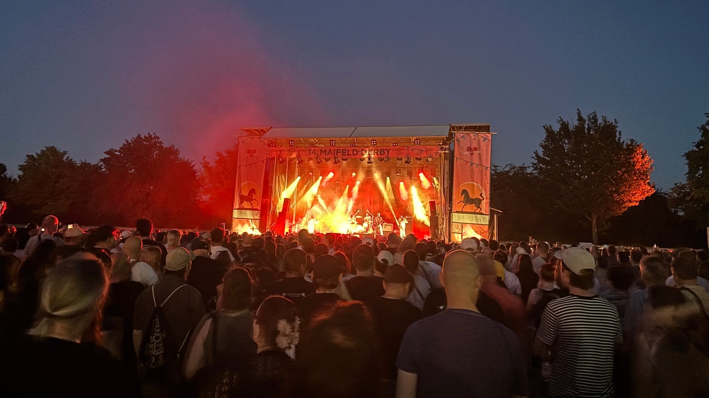 Man sieht eine bunte Bühne. Davor stehen Hunderte Menschen.