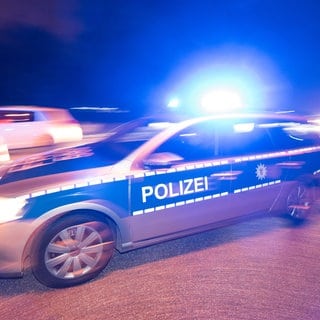 Ein Polizeiauto mit Blaulicht, hinter dem ein Auto schnell vorbeifährt