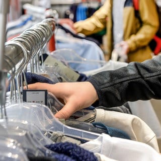 Das Foto zeigt eine Hand die nach Kleidung auf einer Kleiderstange greift. Diebe haben in Rottenburg (Kreis Tübingen) das Modehaus Weippert um mehrere hundert Hosen, Jacken und andere Markenklamotten bestohlen.