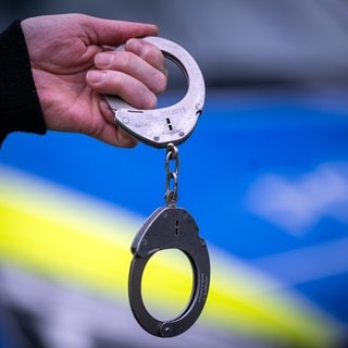 Ein Polizist hält ein Paar Handschellen vor einem Streifenwagen.