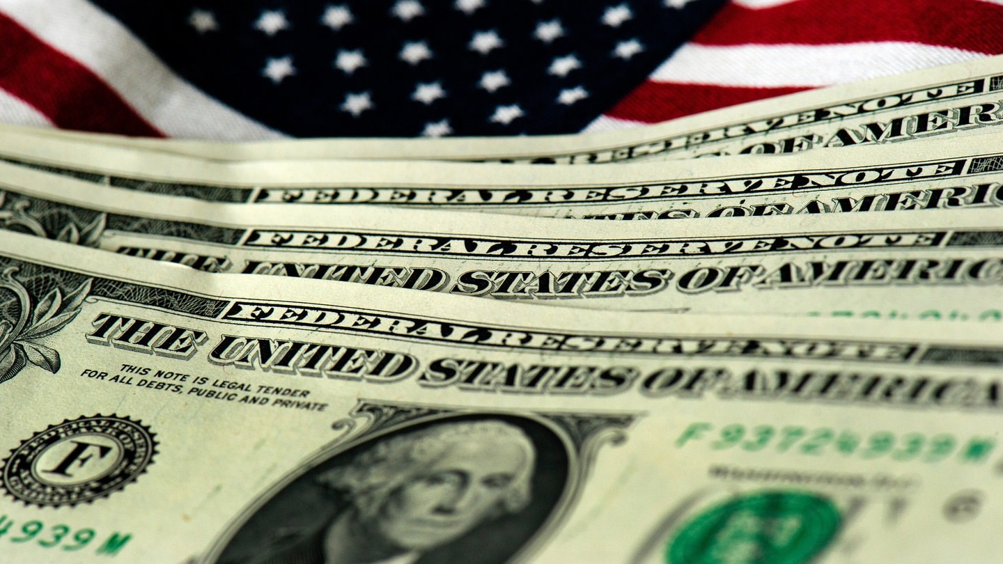 US-amerikanische Geldscheine sind vor einer US-Fahne zu sehen.