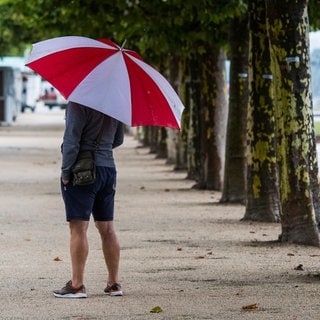 Mann mit Schirm steht im Regen