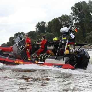 Ein dreiköpfiges DLRG-Team im Einsatzboot fährt über den Rhein - die Kosten zahlt immer wieder die Allgemeinheit.