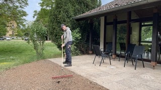 Marco Jungbluth zieht mit einem Rechen die Erde vor der Terrasse ab. Er hat die Terrasse neu gepfalstert. Jetzt fehlt nur noch der Rasen davor.