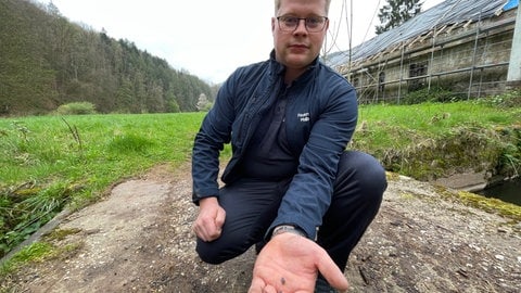 Simon Schloß ärgert sich über das blaue Granulat, dass sich immer noch überall entlang der Kyll findet. (Foto: SWR, Christian Altmayer ) Simon Schloß ärgert sich über das blaue Granulat, dass sich immer noch überall entlang der Kyll findet.