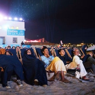 Während der 78. Internationalen Filmfestspiele in Cannes, Südfrankreich, sehen sich Menschen einen Film am Strand an.