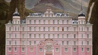 Ein altes, aber luxuriöses Hotel mit pinker Fassade und der Aufschrift "The Grand Budapest Hotel"