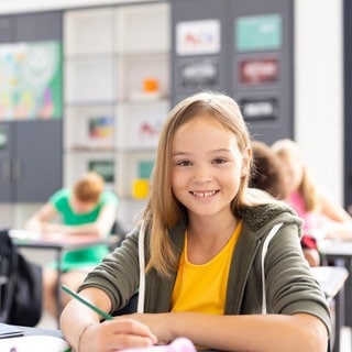 Schülerin arbeitet in der Klasse und lächelt: In Deutschland fehlt eine systematische Datenerhebung, um die Leistungen von Kindern und Jugendlichen wirklich zu verbessern. Gute, individuell erhobene und vernetzte Daten könnten die Leistungen von Schülern verbessern. Kanada oder Estland könnten Vorbild sein.