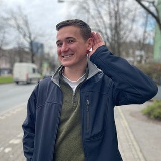 Benedict Kolajka hat selbst eine Hörschädigung und hält lachend eine Hand hinters Ohr: Schlecht hören heißt oft: nicht dazugehören. Mit Schwerhörigkeit steigt das Risiko für Isolation, Depression und Demenz. Trotzdem überspielen viele Betroffene erste Anzeichen aus Scham. Nur wenige steuern mit Hörgeräten gegen. 