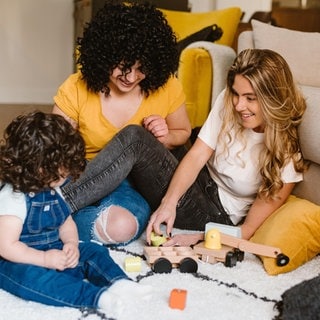 Zwei Mütter spielen mit ihrem Kind: Immer mehr Menschen leben in Patchwork-Familien mit "Bonuskindern", Männer und Frauen ziehen auch ohne Liebesbeziehung zusammen Kinder groß. Die Bundesregierung erarbeitet Vorschläge, um alternative Familienmodelle zu stärken.