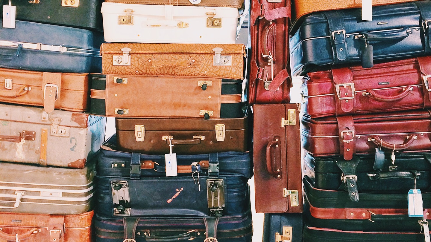 Viele verschiedene Koffer liegen aufeinander auf einem großen Stapel. Wie bekommen Sie Entschädigung und Schadensersatz bei verlorenem Gepäck, verspäteten Flügen, vorverlegten Flügen, Chaos am Flughafen, falschem Hotel und anderen Reisemängeln?